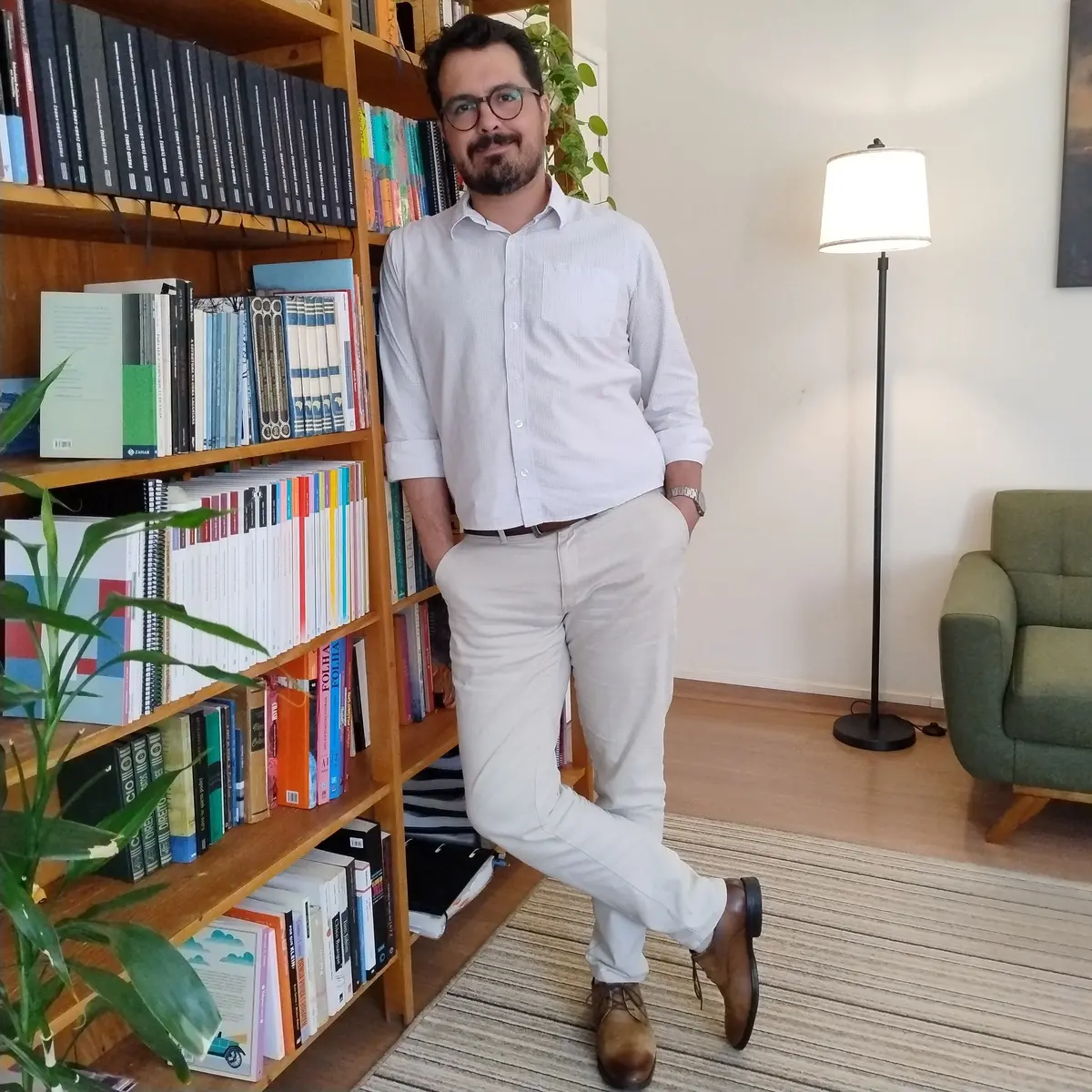 Psicólogo Helder Barbosa em pé ao lado da estante de livros de seu consultório